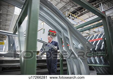 Stock Image - Worker with pressed steel car parts in car factory. Fotosearch