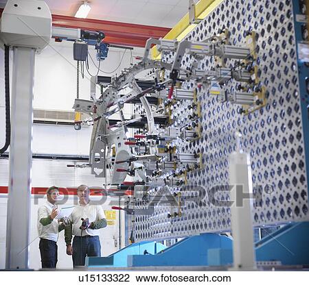 Stock Image - Workers discussing measurement jig for car parts in car factory. Fotosearch