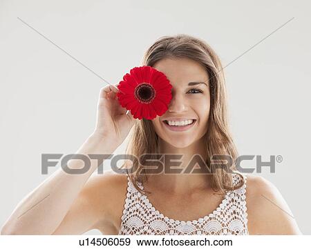 Stock Photo - Beautiful woman holding flower in front of one eye. Fotosearch