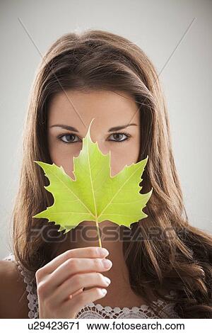 Stock Image - Beautiful woman holding green sycamore leaf in front of mouth and nose. Fotosearch