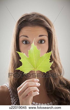 Stock Photography - Beautiful woman holding green sycamore leaf in front of mouth and nose. Fotosearch