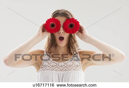 Stock Photograph - Beautiful woman holding two flowers in front of her eyes. Fotosearch