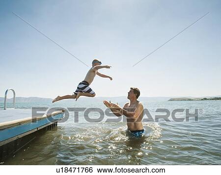 Boy (4-5) jumping into lake caught by his father View Large Photo Image Stock Photograph - Boy (4-5) jumping into lake caught by his father. Fotosearch