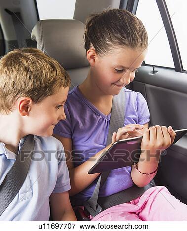 Boy (6-7) and girl (8-9) using digital tablet while sitting in car View Large Photo Image Stock Photo - Boy (6-7) and girl (8-9) using digital tablet while sitting in car. Fotosearch