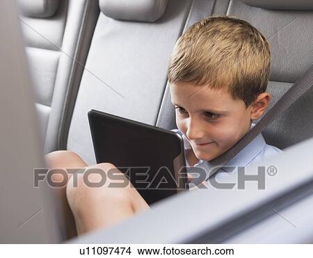 Picture - Boy (6-7) using digital tablet while sitting in car. Fotosearch