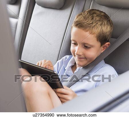 Boy (6-7) using digital tablet while sitting in car View Large Photo Image Stock Image - Boy (6-7) using digital tablet while sitting in car. Fotosearch