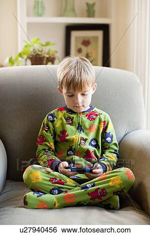 Boy in his pijamas sitting on armchair and playing video game. View Large Photo Image Stock Photograph - Boy in his pijamas sitting on armchair and playing video game.. Fotosearch