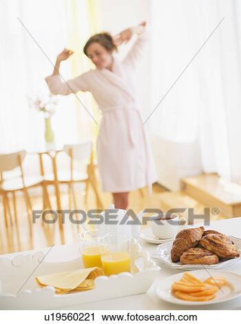 Stock Image - Breakfast scene with woman in white robe stretching. Fotosearch