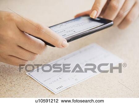 Stock Image - Close up of woman's hand doing online banking with mobile phone. Fotosearch