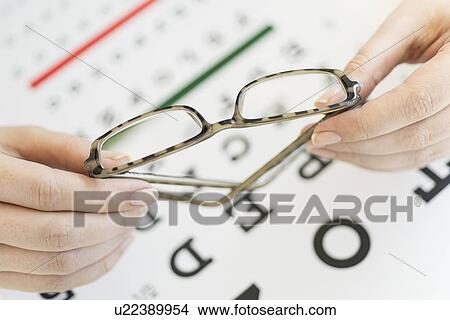 Close up of woman's hands holding glasses above eye chart, studio shot View Large Photo Image Picture - Close up of woman's hands holding glasses above eye chart, studio shot. Fotosearch