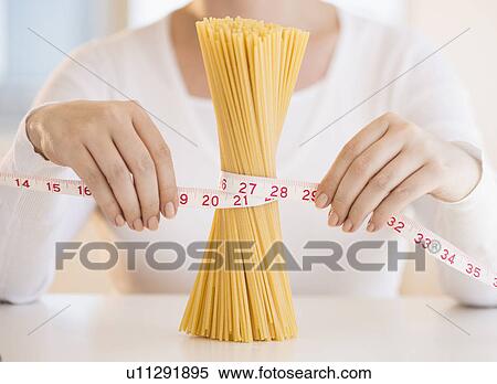 Stock Photography - Close up of woman's hands measuring pasta with tape measure. Fotosearch