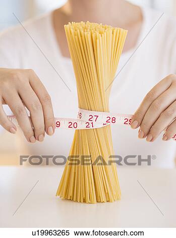Stock Photography - Close up of woman's hands measuring pasta with tape measure. Fotosearch
