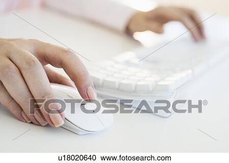 Stock Image - Close up of woman's hands using computer keyboard and computer mouse. Fotosearch