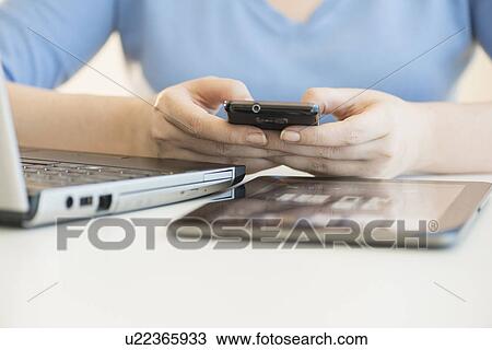 Stock Image - Close up of woman's hands using multiple devices. Fotosearch