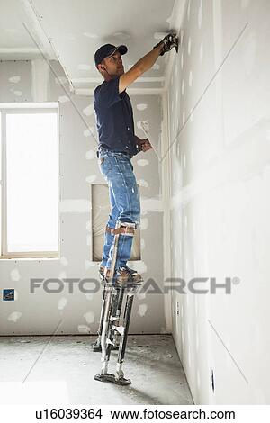 Drywall worker on stilts working on drywall joints View Large Photo Image Picture - Drywall worker on stilts working on drywall joints. Fotosearch