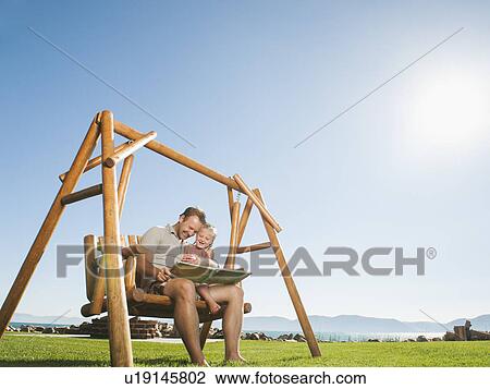 Father with daughter (4-5) on swing reading book View Large Photo Image Stock Image - Father with daughter (4-5) on swing reading book. Fotosearch