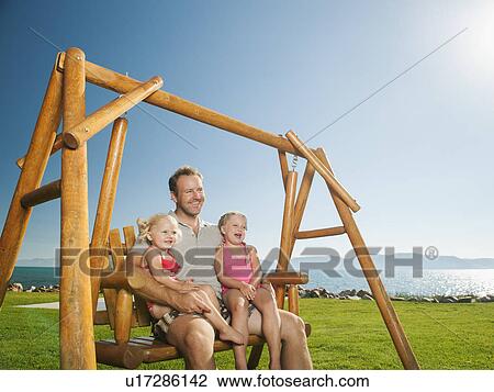 Stock Image - Father with daughters (2-3, 4-5) on swing. Fotosearch