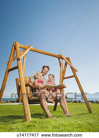 Father with daughters (2-3, 4-5) on swing reading book View Large Photo Image Stock Photo - Father with daughters (2-3, 4-5) on swing reading book. Fotosearch