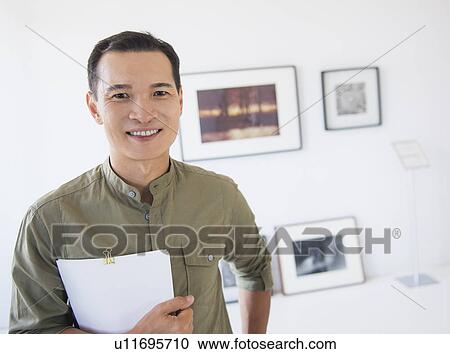 Stock Image - Gallery worker posing in front of newly hanged paintings. Fotosearch