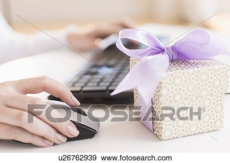 Gift box on desk next to woman using computer View Large Photo Image Stock Photo - Gift box on desk next to woman using computer. Fotosearch