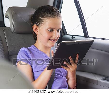 Stock Photo - Girl (8-9) using digital tablet while sitting in car. Fotosearch