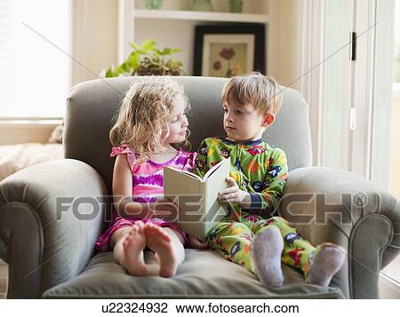 Stock Image - Girl and boy sitting on armchair and holding book. Fotosearch
