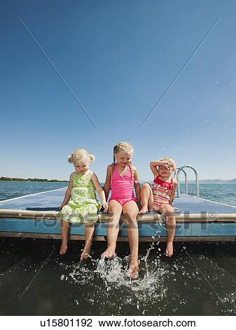 Stock Image - Girls (2-3, 4-5) sitting at the edge of raft and splashing water. Fotosearch