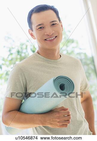 Picture - Happy mid adult man holding exercising mat. Fotosearch