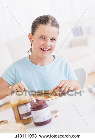 Stock Image - Happy young girl (8-9) having breakfast. Fotosearch