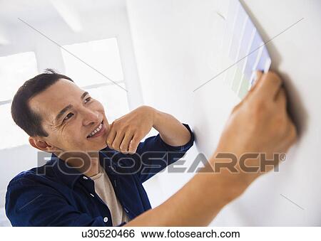 Stock Photograph - Man applying paint samples to white wall. Fotosearch