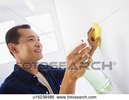 Stock Photograph - Man washing white walls with spray and yellow sponge. Fotosearch
