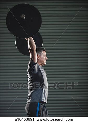 Stock Image - Mature man lifting heavy barbell . Fotosearch