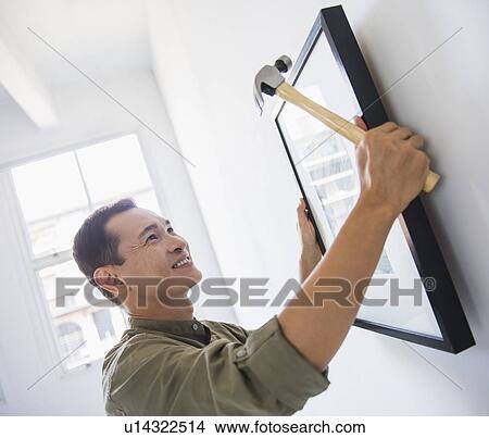 Mid adult man hanging picture on wall View Large Photo Image Picture - Mid adult man hanging picture on wall. Fotosearch