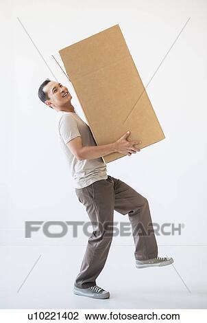 Stock Image - Mid adult moving cardboard heavy box. Fotosearch