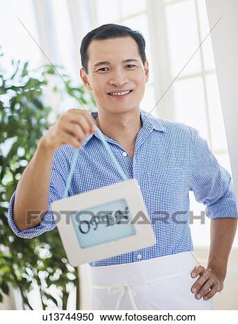 Stock Image - Mid adult waiter holding open sign. Fotosearch