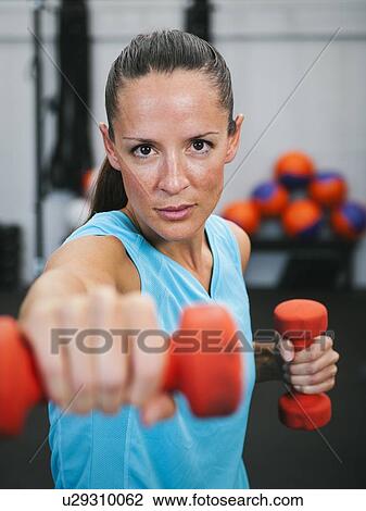 Mid adult woman exercising with dumbbells View Large Photo Image Stock Image - Mid adult woman exercising with dumbbells. Fotosearch