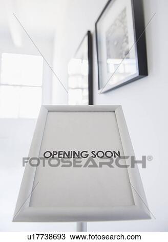 Stock Image - Opening sign with pictures on white wall in background. Fotosearch