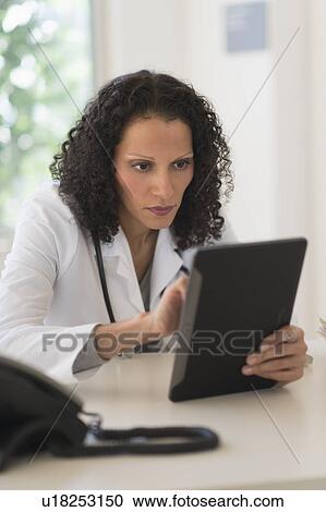 Stock Image - Portrait of doctor sitting in office and using digital tablet. Fotosearch