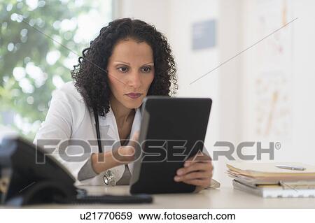 Stock Photo - Portrait of doctor sitting in office and using digital tablet. Fotosearch