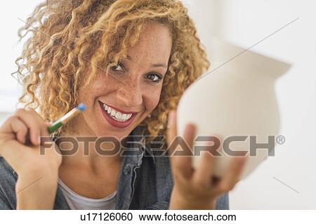 Stock Image - Portrait of female artist painting on ceramics in studio. Fotosearch