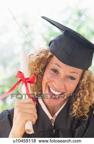 Stock Photo - Portrait of smiling young woman in mortarboard showing diploma. Fotosearch