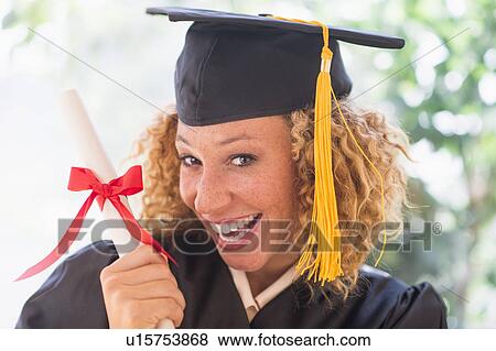 Stock Photo - Portrait of smiling young woman in mortarboard showing diploma. Fotosearch