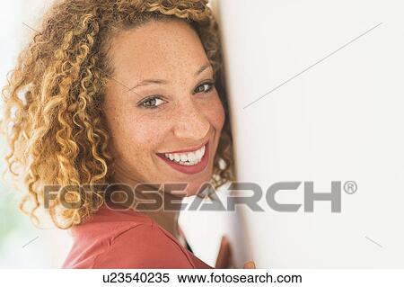 Stock Photography - Portrait of smiling young woman near wall. Fotosearch