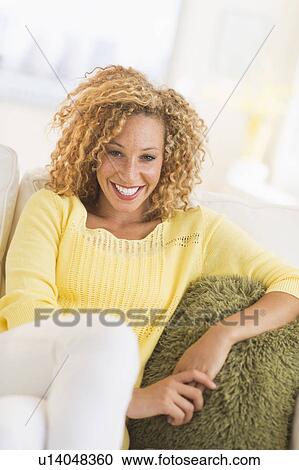 Portrait of smiling young woman sitting on sofa View Large Photo Image Stock Image - Portrait of smiling young woman sitting on sofa. Fotosearch