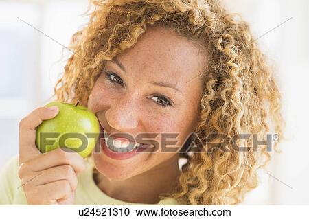 Stock Image - Portrait of smiling young woman with apple. Fotosearch