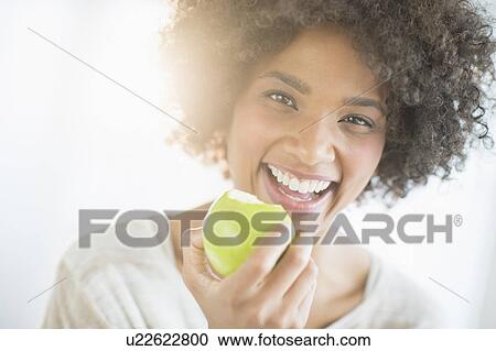 Stock Image - Portrait of woman eating apple, studio shot. Fotosearch