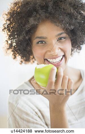 Stock Photo - Portrait of woman eating apple, studio shot. Fotosearch