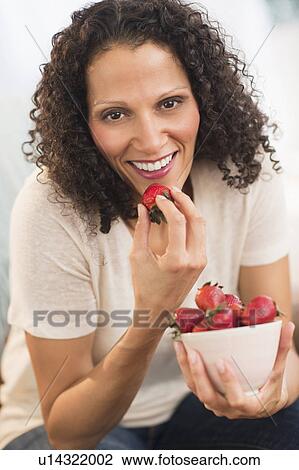 Stock Image - Portrait of woman eating strawberries. Fotosearch
