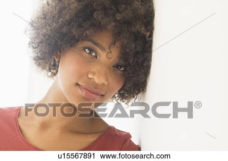 Stock Image - Portrait of woman leaning against wall, studio shot. Fotosearch