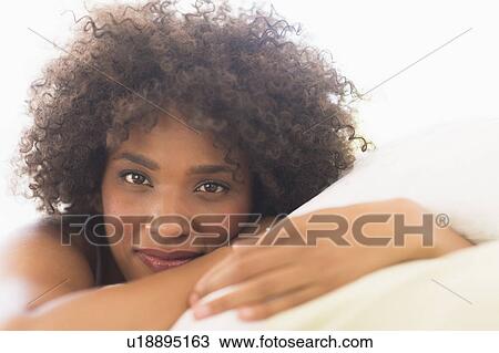 Stock Image - Portrait of woman lying on bed. Fotosearch